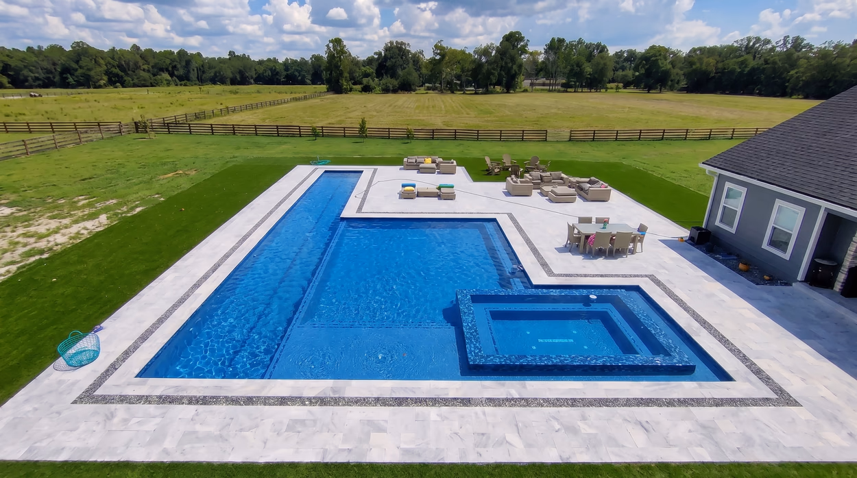 Large geometric pool with a sun shelf and raised spa on open North Florida acreage, framed by a banded marble deck.