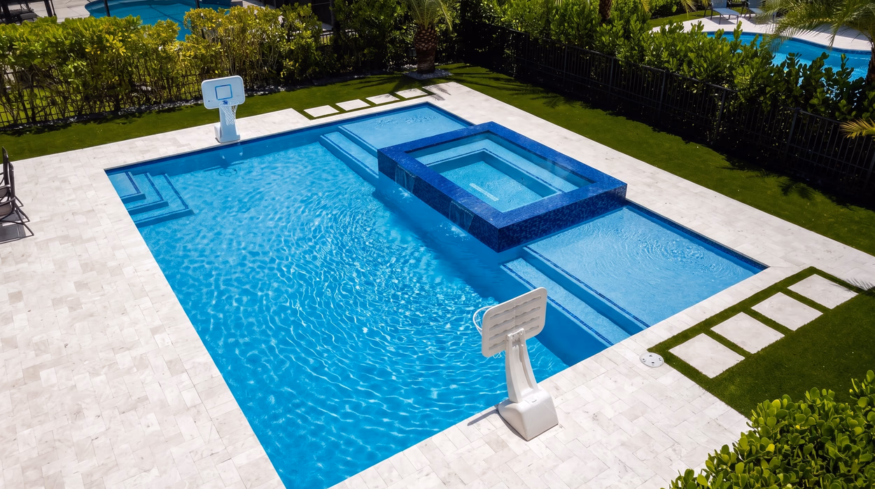 Rectangular pool with a raised spa and travertine deck in South Florida, built by Mr & Mrs Outdoor Living