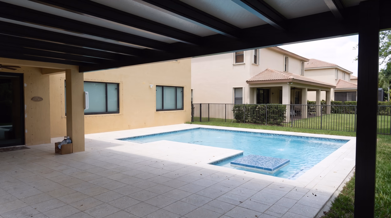 Pool and spa seen from the covered patio, looking out across the travertine deck.
